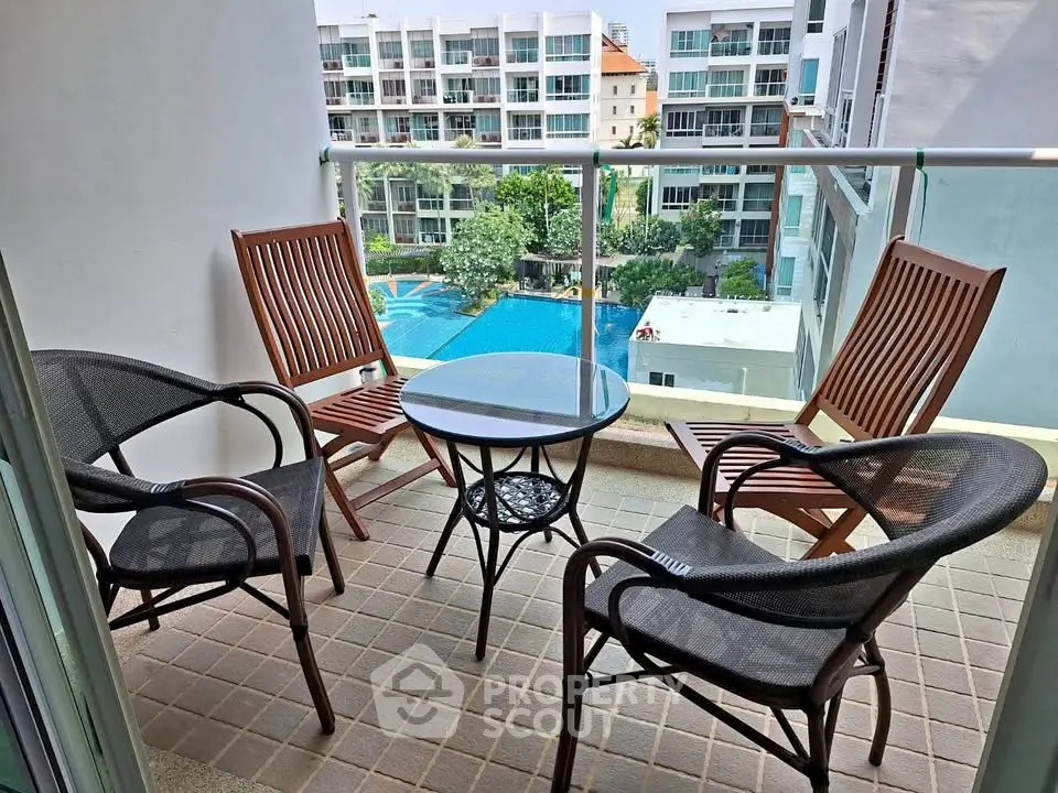 Charming balcony with stylish seating and pool view in modern apartment complex.
