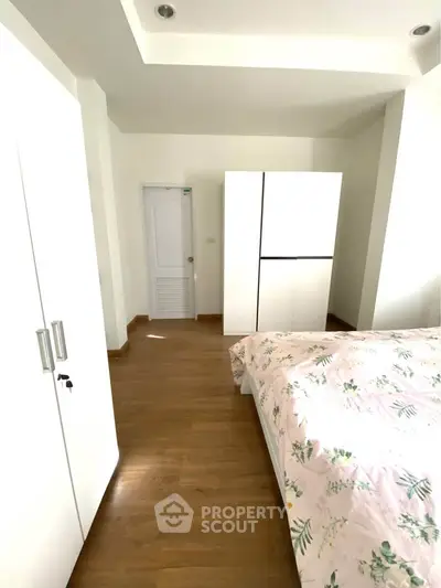 Bright bedroom with wooden flooring and white wardrobes, featuring a cozy bed with floral bedding.