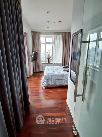 Modern bedroom with wooden flooring and large window offering city views.