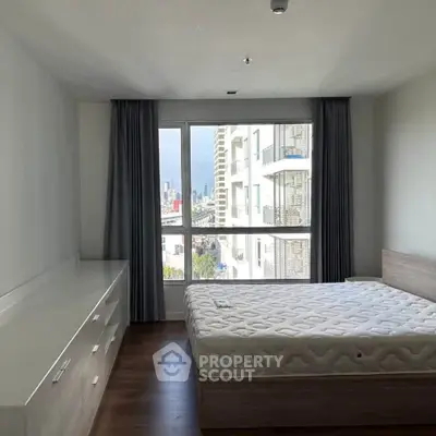 Spacious bedroom with large window offering city view, featuring modern furniture and hardwood flooring.