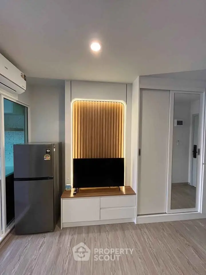 Modern living room with sleek TV unit and stylish lighting, featuring a refrigerator and mirrored wardrobe.