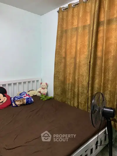 Cozy bedroom with brown bedding and decorative curtains, featuring a fan and plush toys for a homely touch.