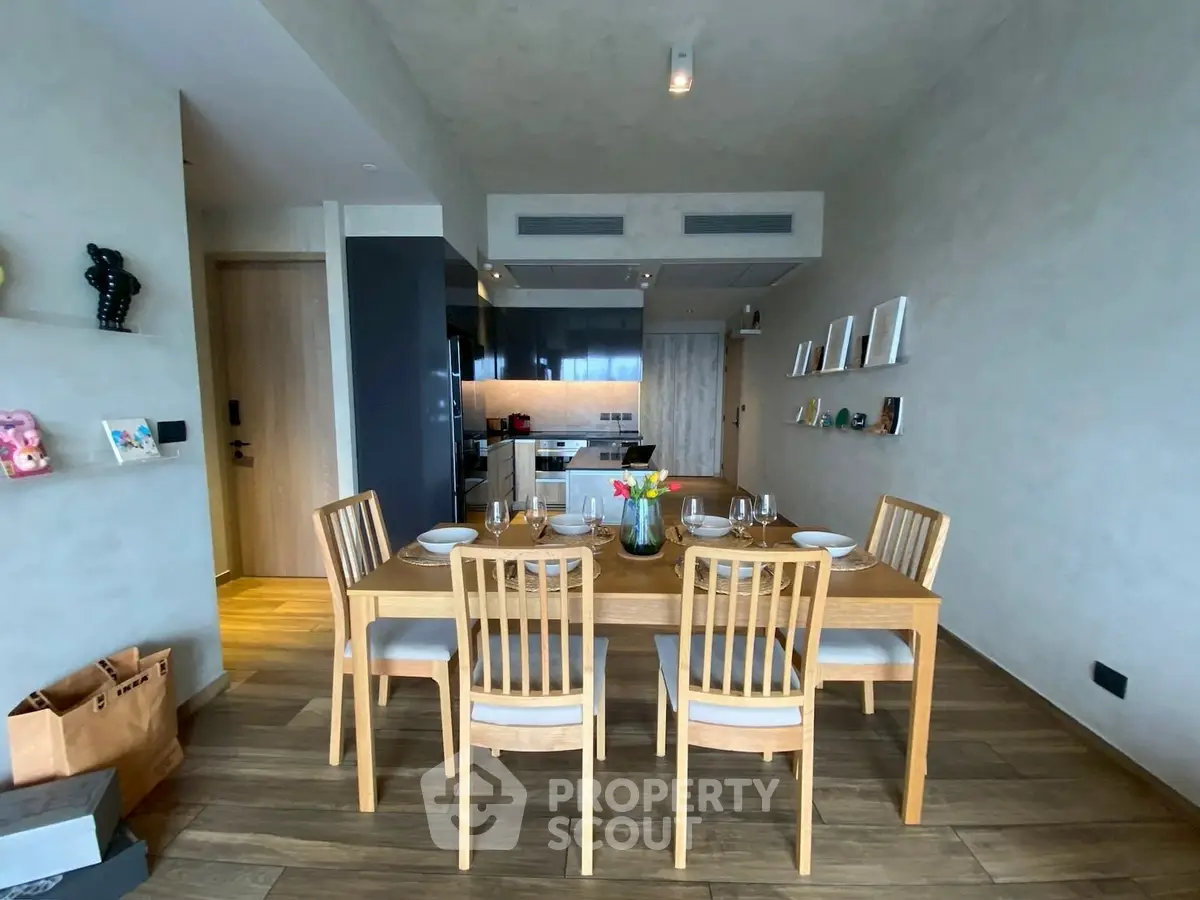 Modern dining area with wooden table and chairs, stylish decor, and open kitchen layout.