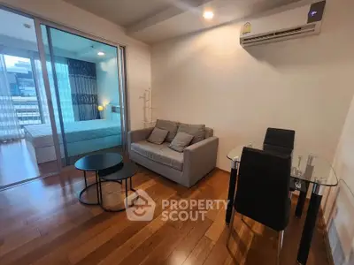 Modern living room with wooden flooring, cozy sofa, and glass dining table in open layout apartment.