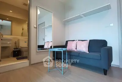 Modern living room with stylish sofa and mirror, adjacent to a compact bathroom.