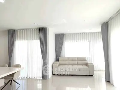 Spacious living room with elegant white sofa and floor-to-ceiling windows with gray curtains.
