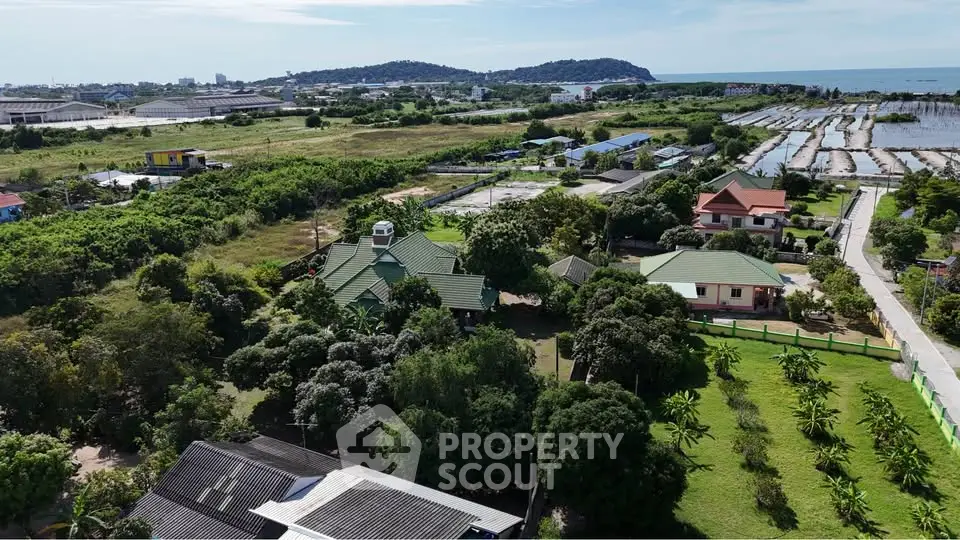 Scenic aerial view of lush green landscape with houses and distant ocean, perfect for serene living.