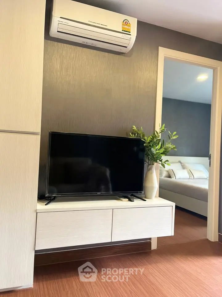 Modern living room with sleek TV setup and air conditioning, leading to a cozy bedroom.