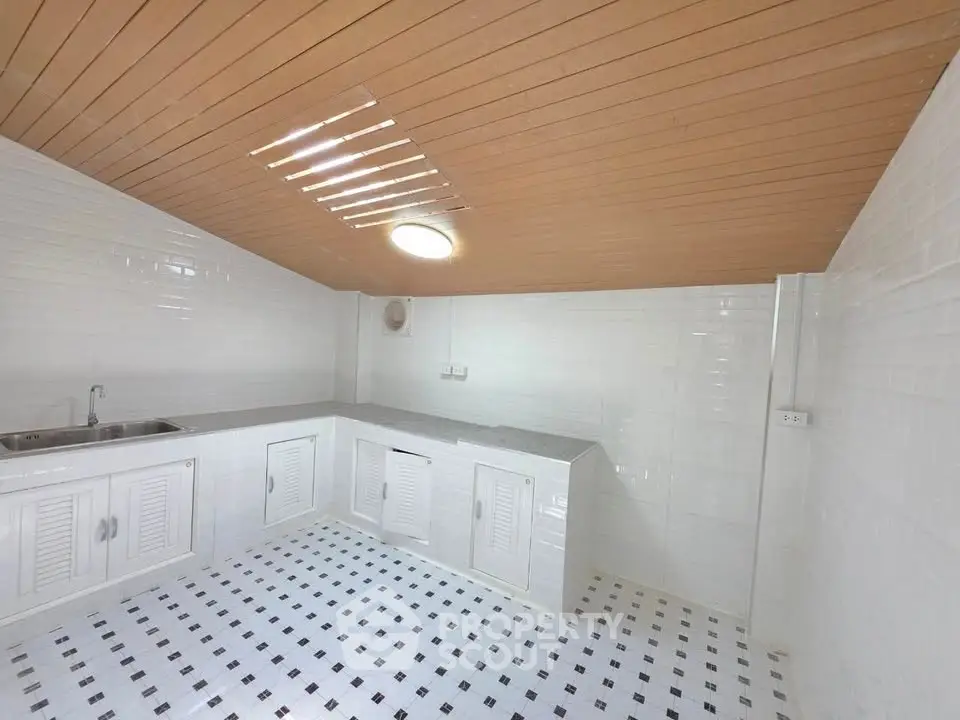 Modern kitchen with white tiled walls and wooden ceiling, featuring a sleek countertop and sink.