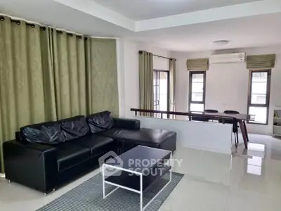 Spacious modern living room with black leather sofa and dining area, featuring large windows and elegant curtains.
