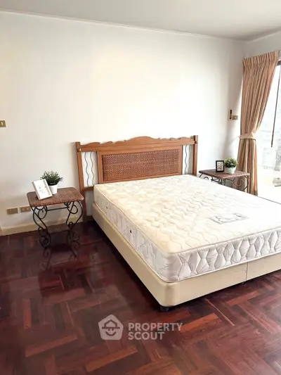 Spacious bedroom with wooden flooring and large window for natural light.