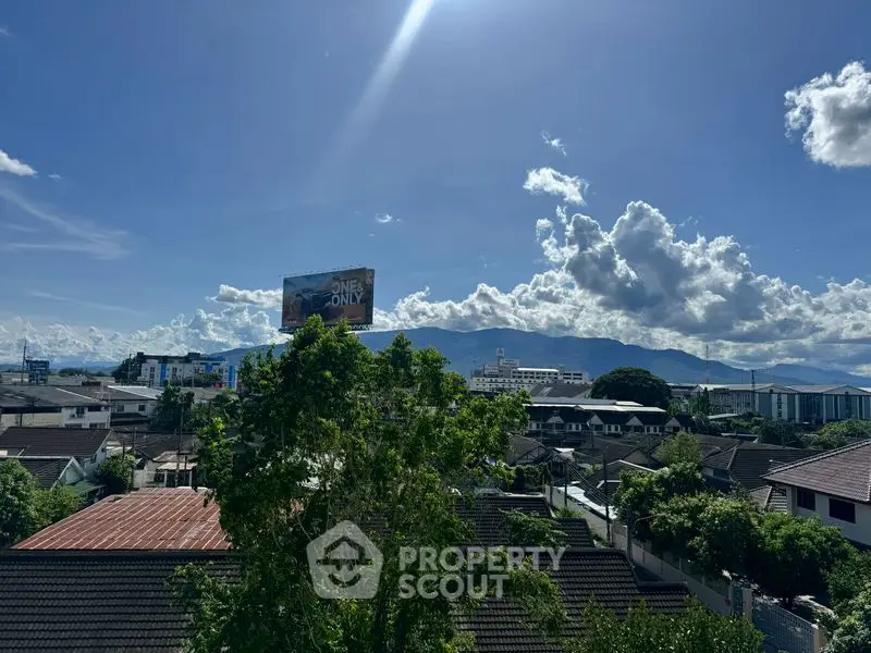 Scenic cityscape view with mountains and residential rooftops under a clear blue sky.
