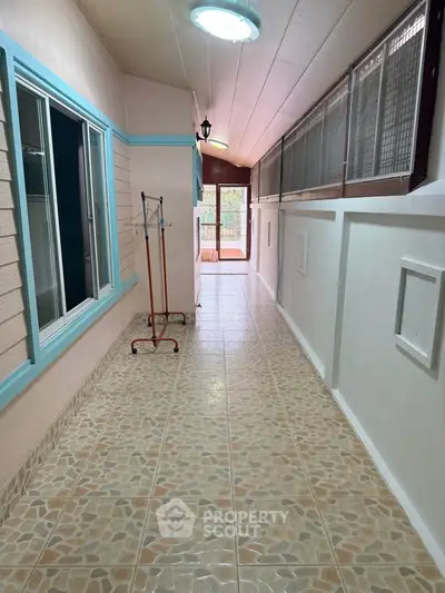 Bright corridor with tiled flooring and large windows leading to a balcony.