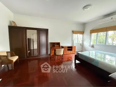 Spacious bedroom with wooden flooring and large windows offering natural light.
