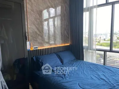 Modern bedroom with large window and city view, featuring stylish decor and cozy bedding.