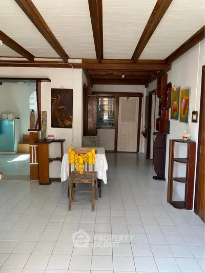 Charming open-layout living space with rustic wooden beams and artistic decor, perfect for cozy gatherings.