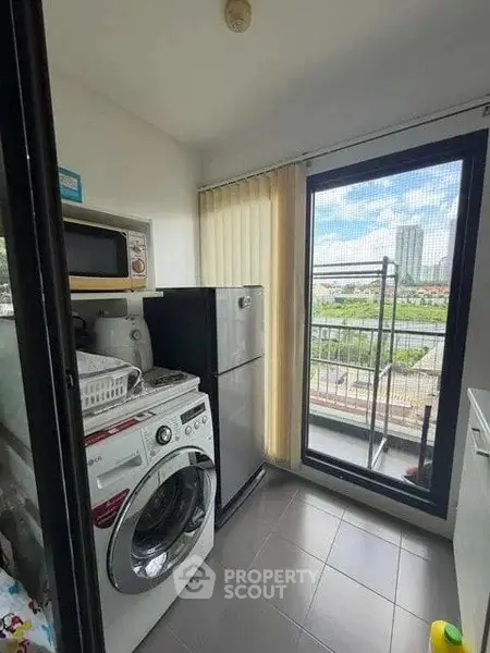 Compact laundry area with washing machine, microwave, and fridge near balcony with city view.
