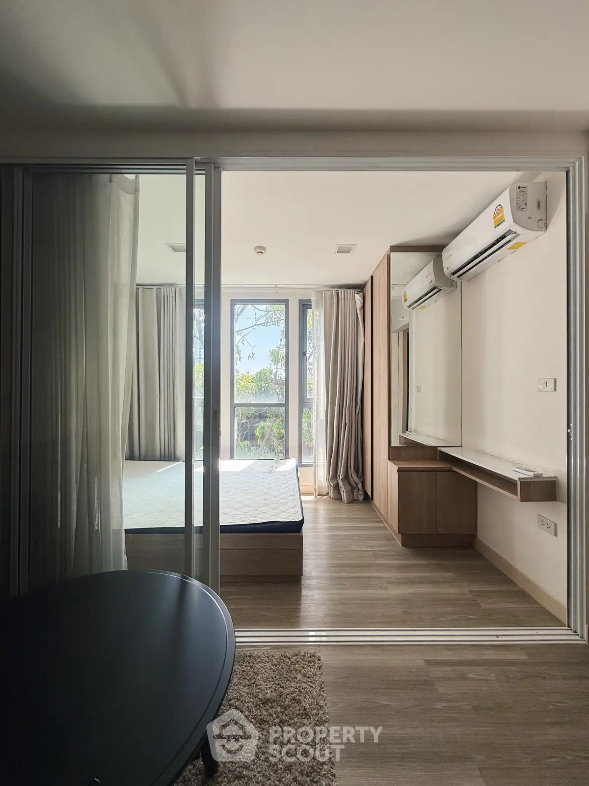 Spacious bedroom with large windows and modern air conditioning, featuring a serene view and elegant wooden flooring.