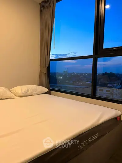 Cozy bedroom with large window offering stunning city view at dusk.