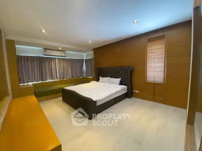 Spacious bedroom with modern design and natural light, featuring a stylish bed and wooden accents.