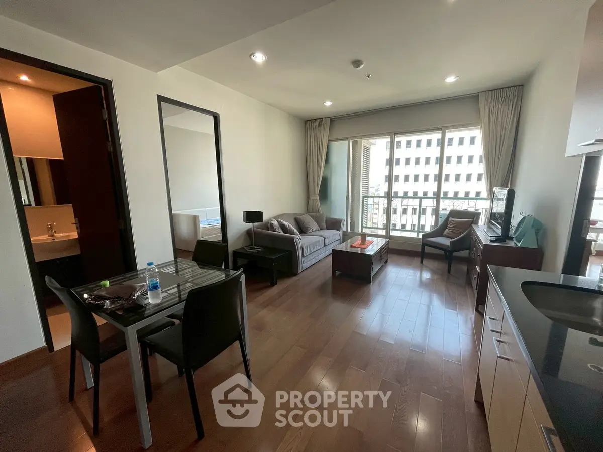 Modern living room with wooden flooring, large windows, and stylish furniture in a city apartment.