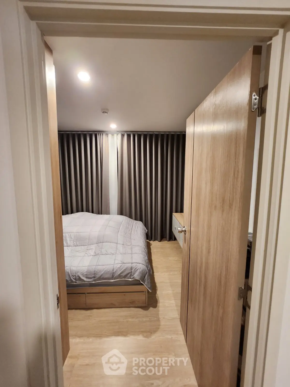 Cozy bedroom with wooden flooring and modern decor, featuring a comfortable bed and elegant curtains.