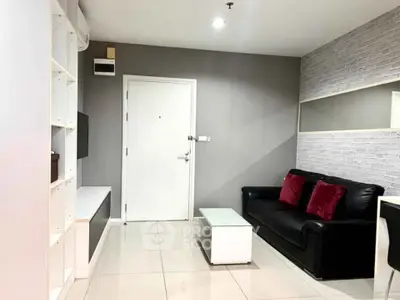 Modern living room with sleek black sofa, white shelving, and stylish decor in a contemporary apartment.