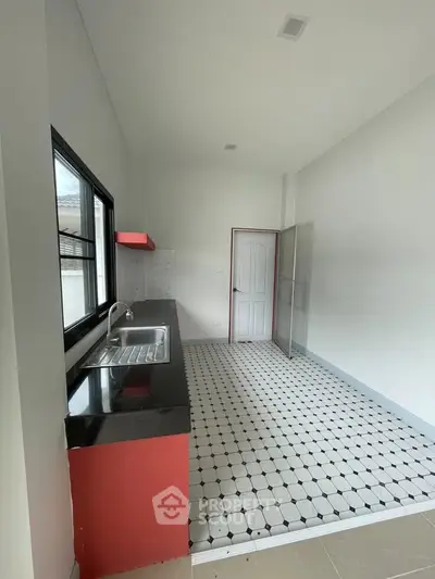 Modern kitchen with sleek black countertops and red accents, featuring a spacious layout and large window.