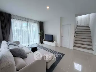 Modern living room with cozy sofa, sleek TV setup, and elegant staircase in bright, airy space.