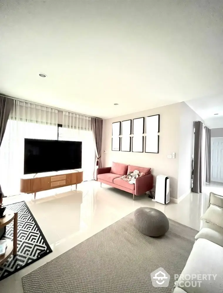 Spacious and modern living room with sleek white walls, a plush red sofa, and a large flat-screen TV, bathed in natural light from floor-to-ceiling windows.