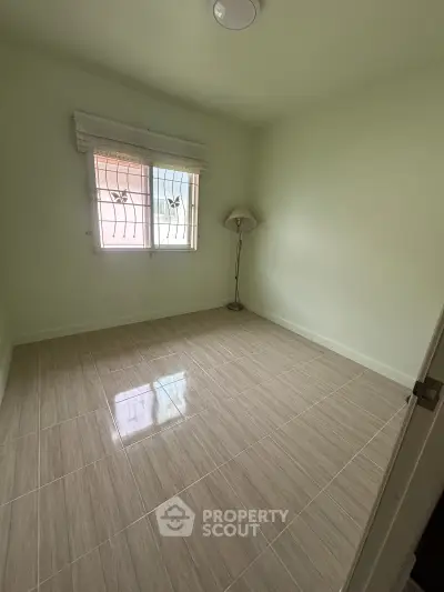 Spacious empty bedroom with tiled flooring and natural light from window, perfect for customization.