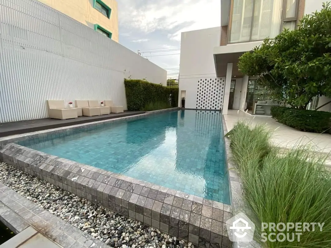 Luxurious private pool with mosaic tiles and modern architecture, surrounded by lush greenery and elegant outdoor seating, perfect for upscale living.