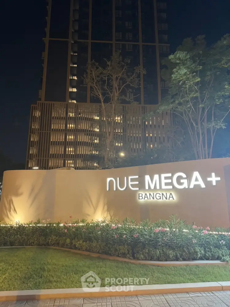 Stunning night view of Nue Mega Plus Bangna building with illuminated sign and lush landscaping.