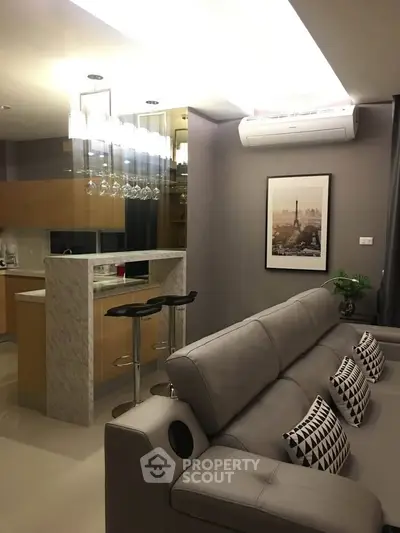 Modern living room with stylish decor and open kitchen layout, featuring a cozy sofa and elegant lighting.