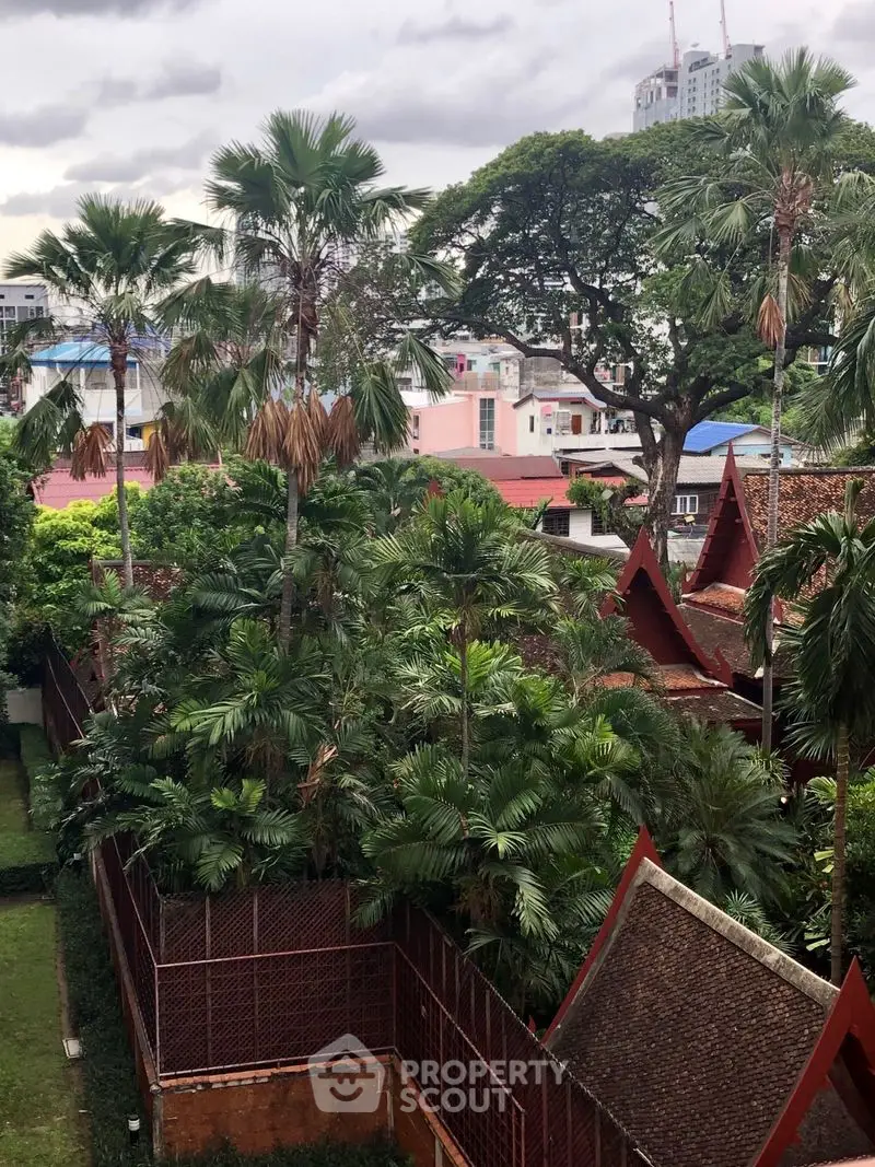 Lush tropical garden view with traditional architecture and city skyline backdrop.