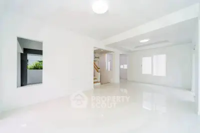 Spacious modern living room with white walls and glossy floors, featuring large windows for natural light.