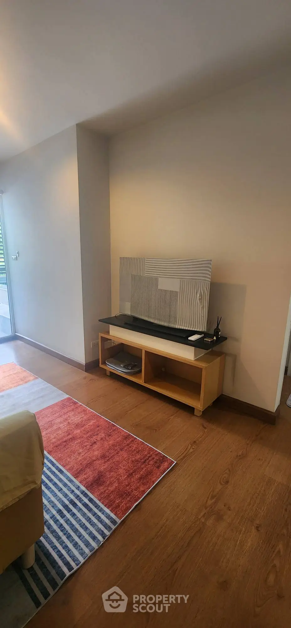 Spacious living room with modern decor and wooden flooring, featuring a stylish TV stand and vibrant area rug.