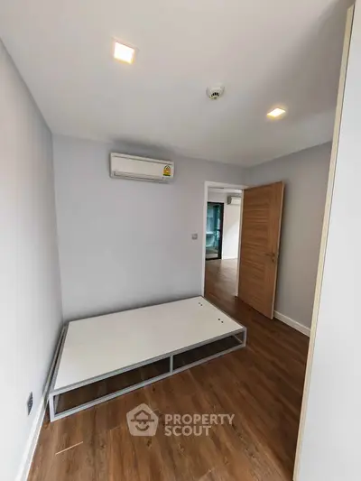 Modern minimalist bedroom with wooden flooring and air conditioning unit.