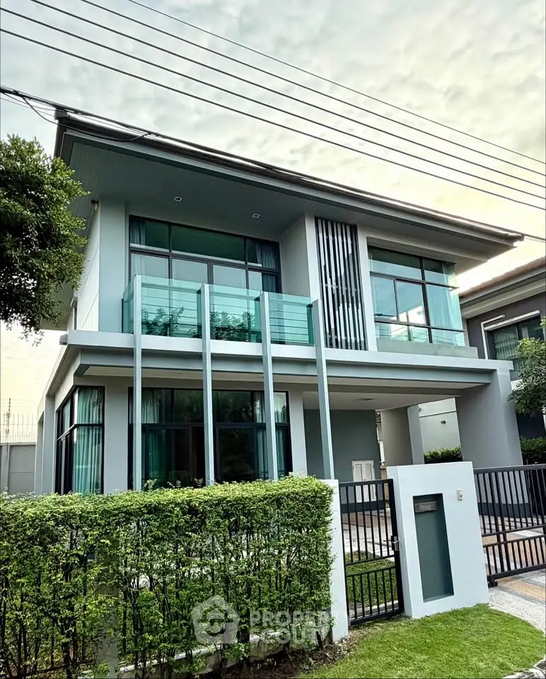 Modern two-story house with glass balcony and lush greenery