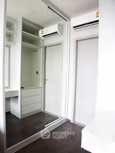 Modern bedroom with mirrored closet and air conditioning unit, featuring sleek design and ample storage space.
