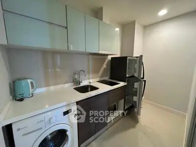 Modern kitchen with sleek cabinets, washing machine, and fridge in compact layout.