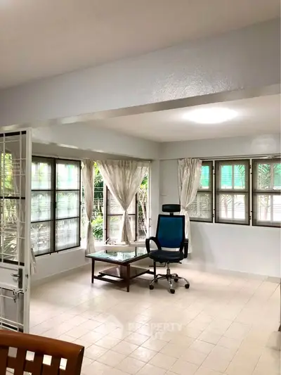 Spacious living room with large windows and natural light, featuring a modern chair and glass coffee table.
