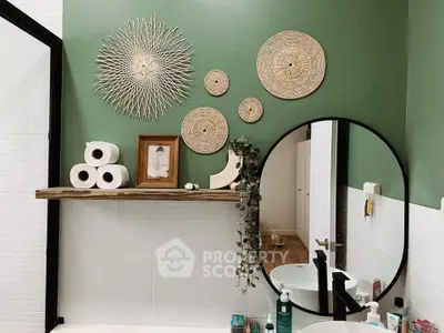 Stylish bathroom with green accent wall, round mirror, and decorative wall art.