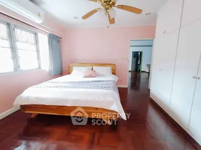 Cozy bedroom with wooden bed and built-in wardrobe, featuring pink walls and ceiling fan.