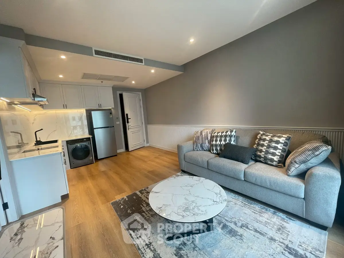 Modern living room with stylish decor, featuring a cozy sofa, marble coffee table, and compact kitchen area.
