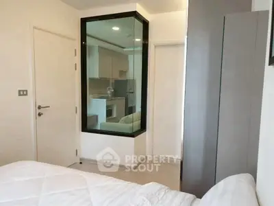 Modern bedroom with glass partition overlooking a sleek kitchen area.