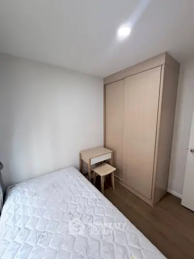 Cozy bedroom with minimalist design featuring a bed, wooden wardrobe, and small desk with stool.