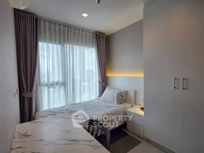 Cozy bedroom with modern decor and large window offering city views, perfect for urban living.