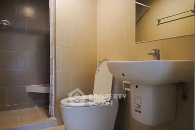 Modern bathroom with sleek fixtures and neutral tiles, featuring a shower and toilet.