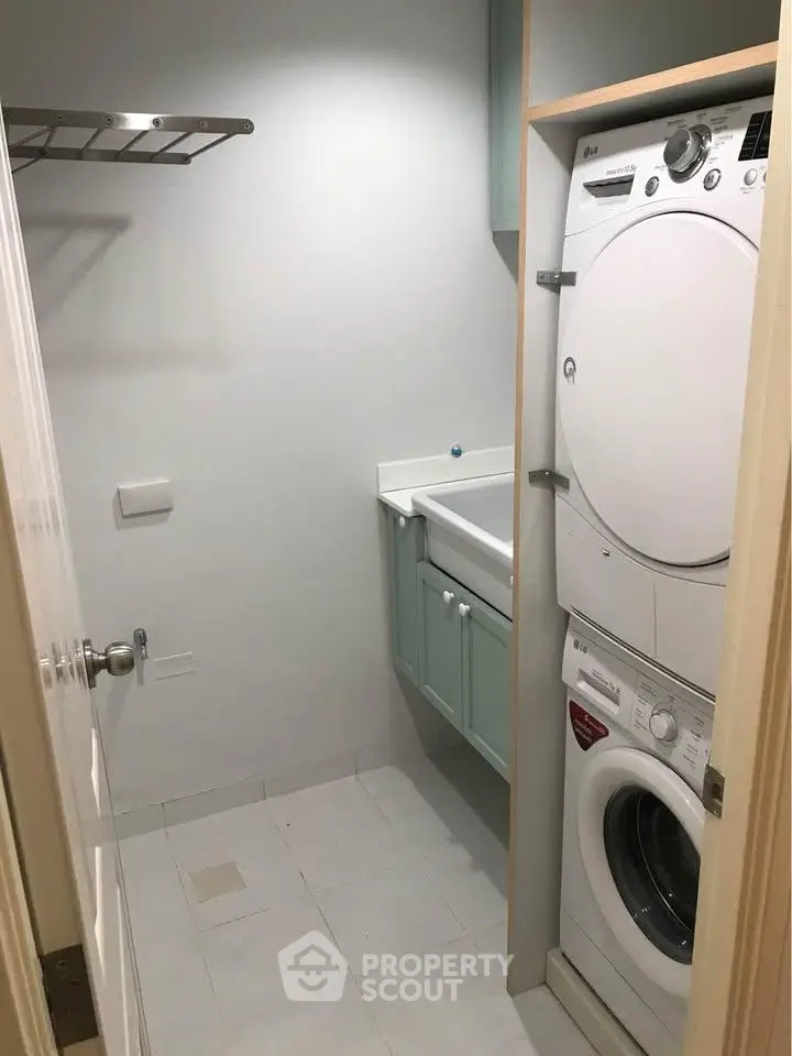 Compact laundry room with stacked washer and dryer, wall-mounted shelf, and utility sink.